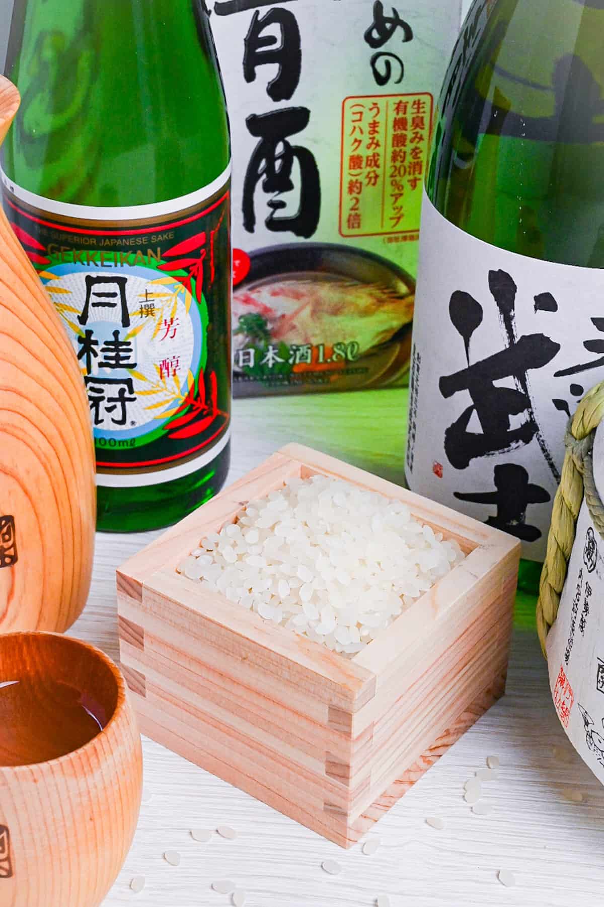 rice in a wooden box surrounded by various bottles of sake