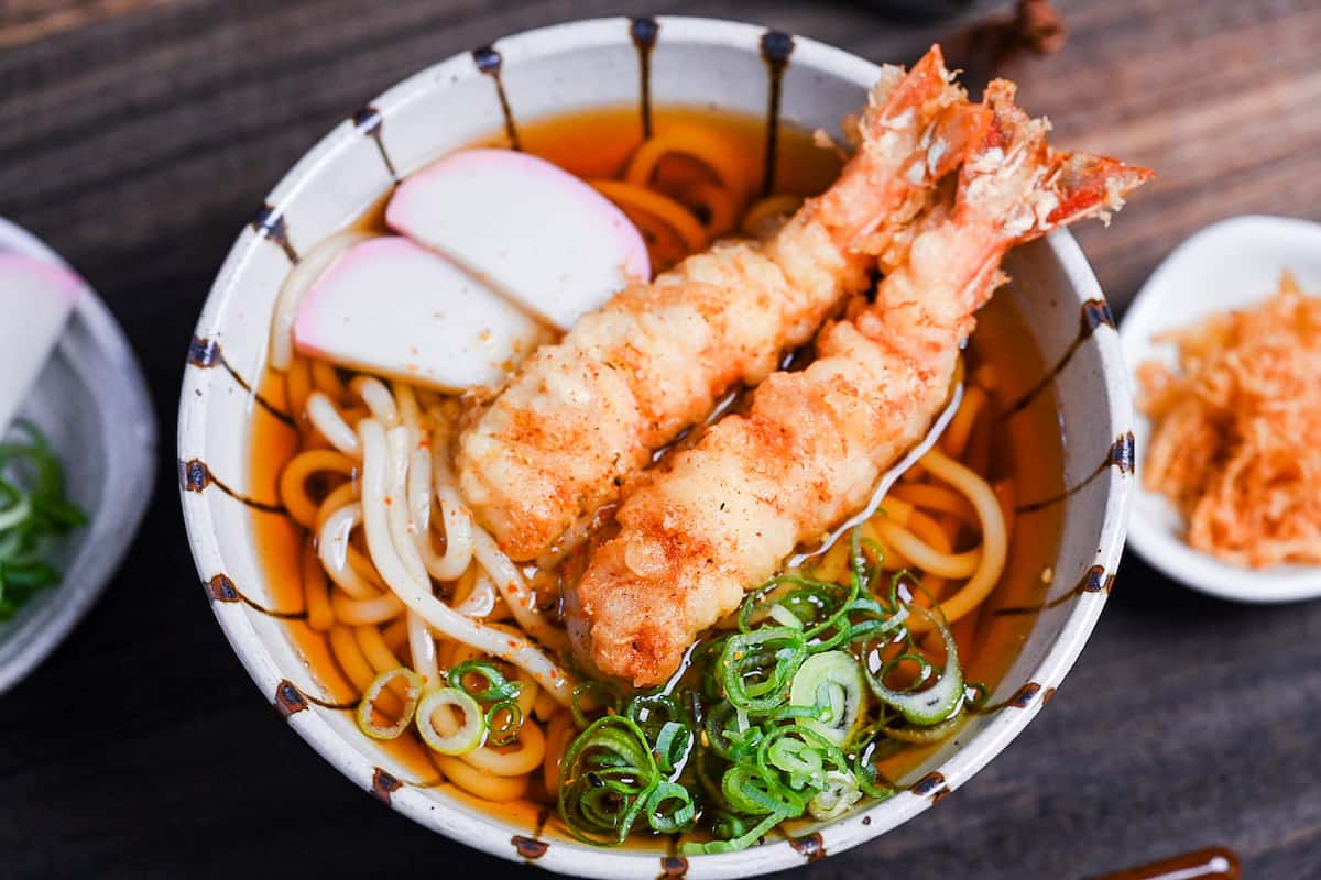 Ebiten Udon - Homemade udon noodle soup in a stripy bowl topped with kamaboko, green onion and tempura shrimp