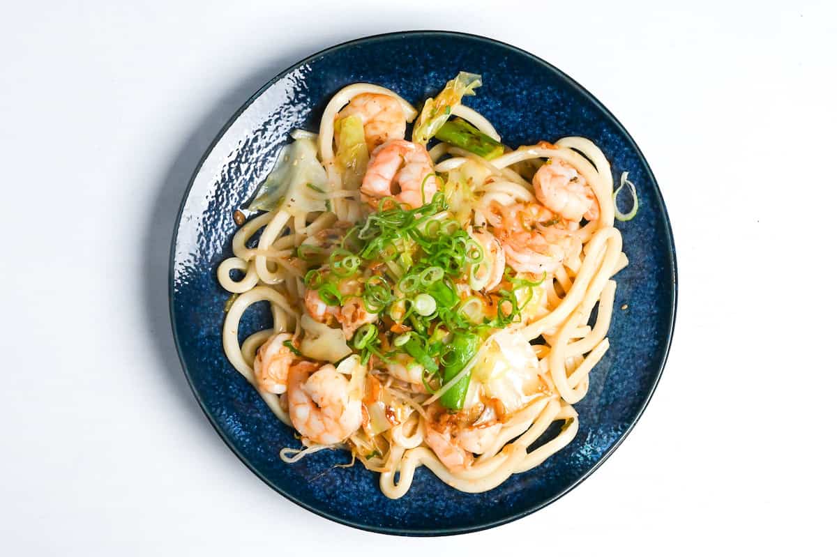 shrimp yaki udon on a blue plate topped with finely sliced green onions
