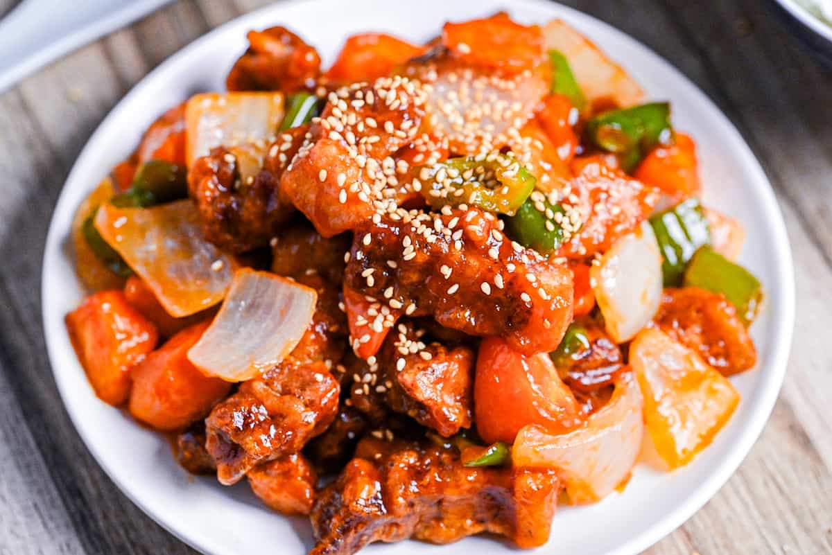 Subuta (Japanese sweet and sour pork) on a white plate sprinkled with white sesame seeds