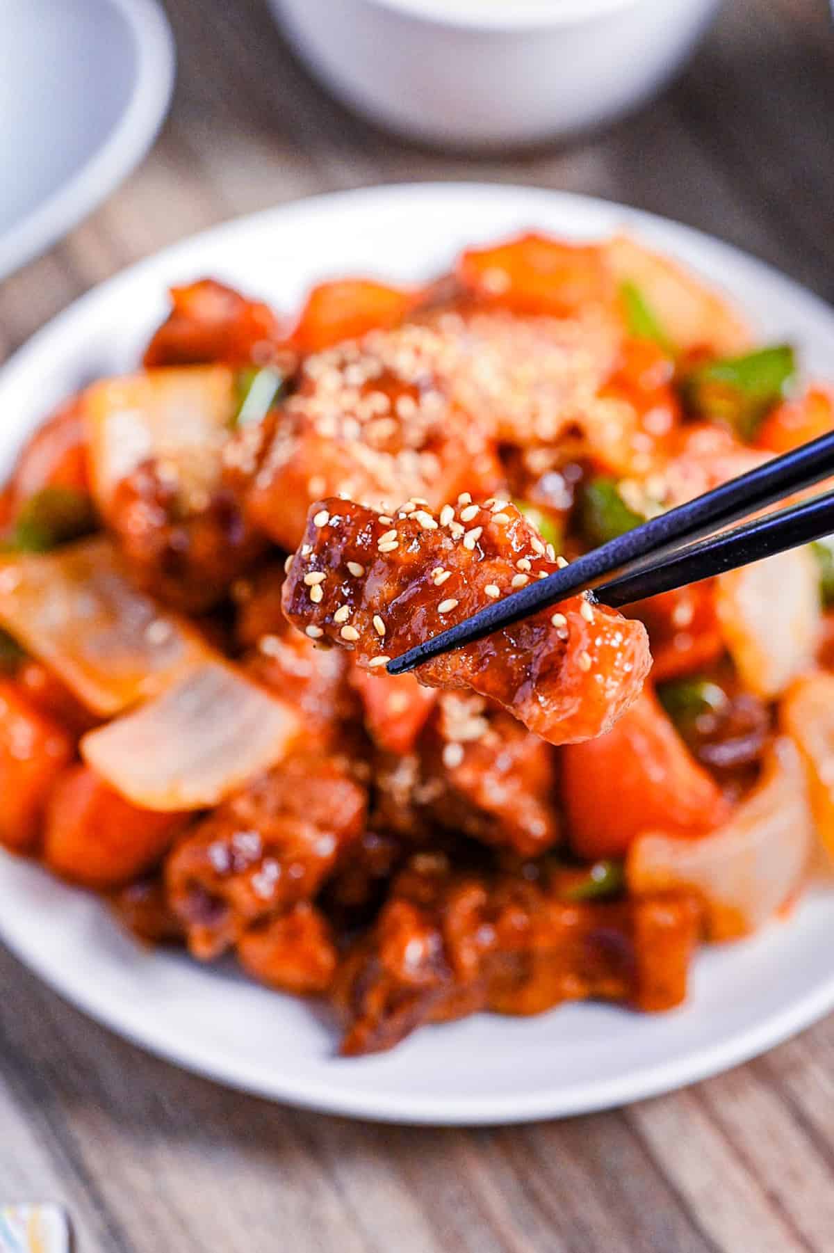 a close up of subuta (Japanese sweet and sour pork) held with black chopsticks