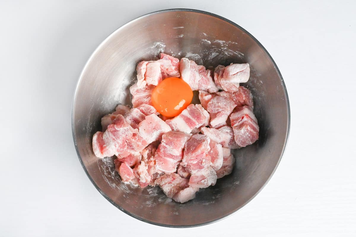 pieces of flour coated pork belly in a mixing bowl with a raw egg yolk
