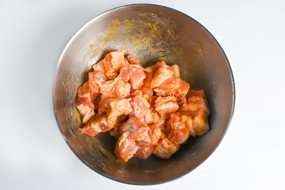 cubes of pork belly coated in flour and egg yolk in a steel mixing bowl