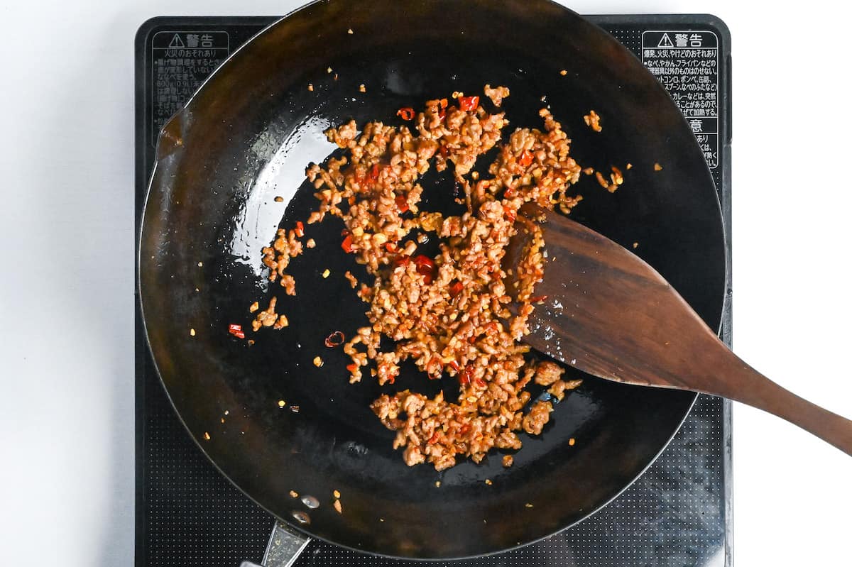 ground pork frying in a wok with thinly sliced dry red chili