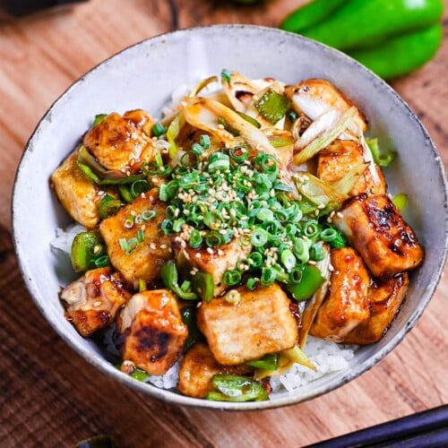 tofu donburi with teriyaki glaze topped with chili oil, green onion and sesame seeds over rice in a mottled bowl