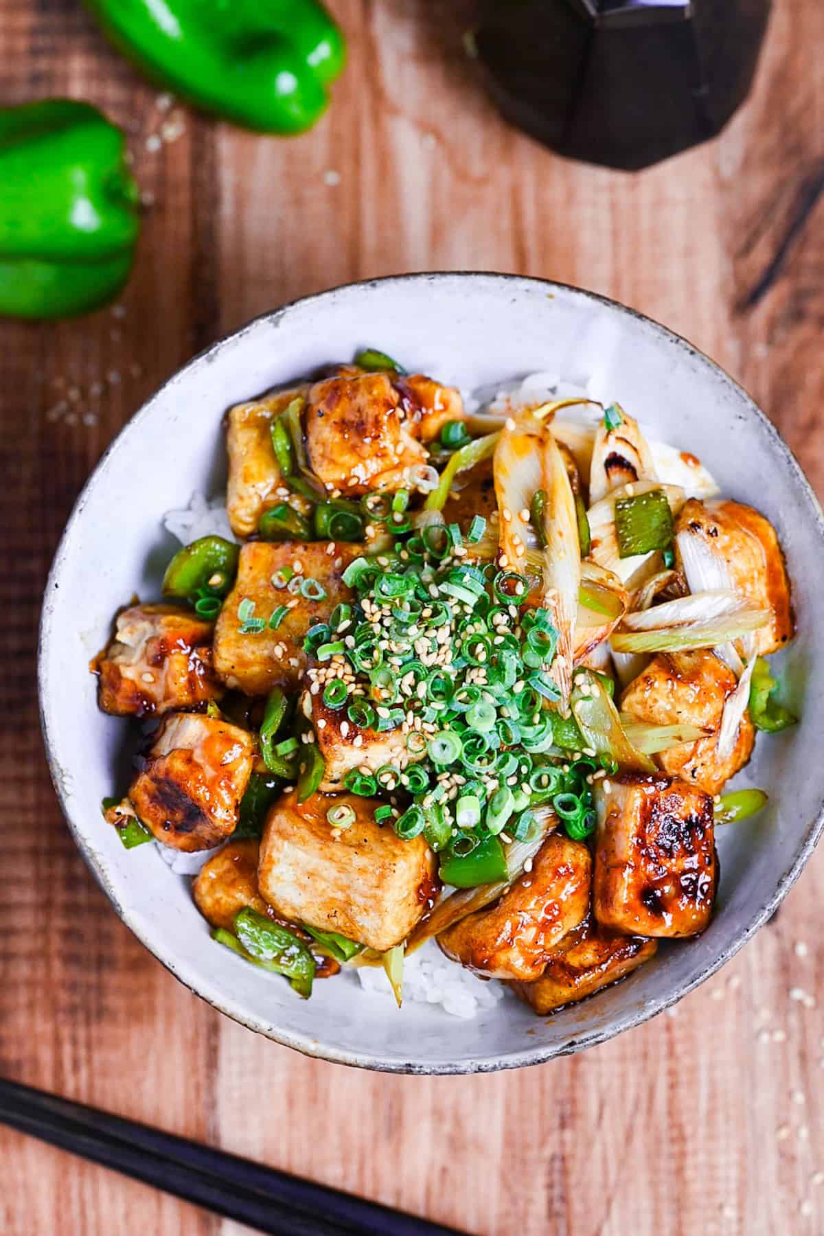 tofu donburi with teriyaki glaze topped with chili oil, green onion and sesame seeds over rice in a mottled bowl