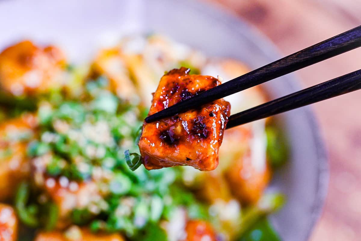 close up of teriyaki tofu held with black chopsticks