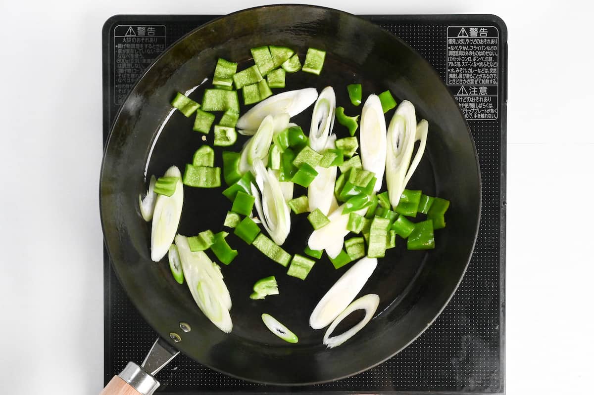 green bell peppers and green onions frying in a pan