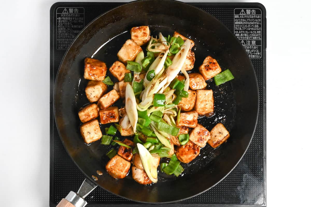 teriyaki glazed tofu in a pan with green onion and bell peppers