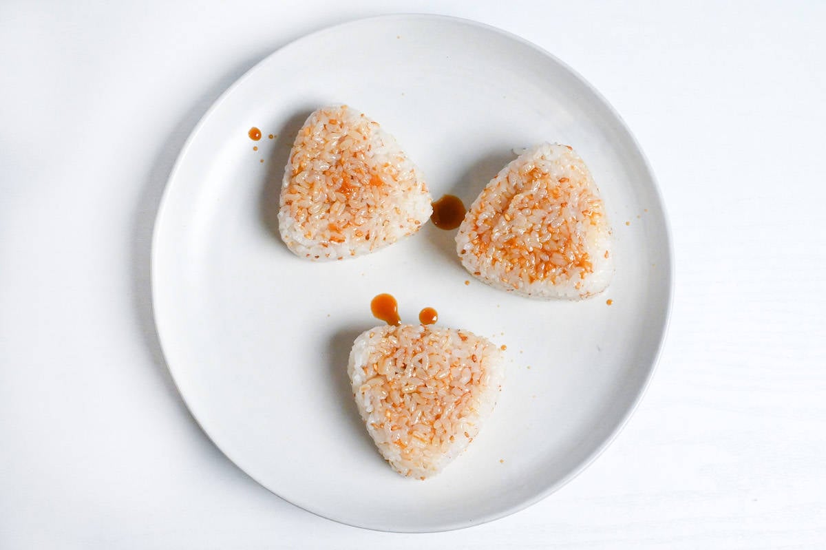 the front and back of three yaki onigiri brushed with sauce on a white plate