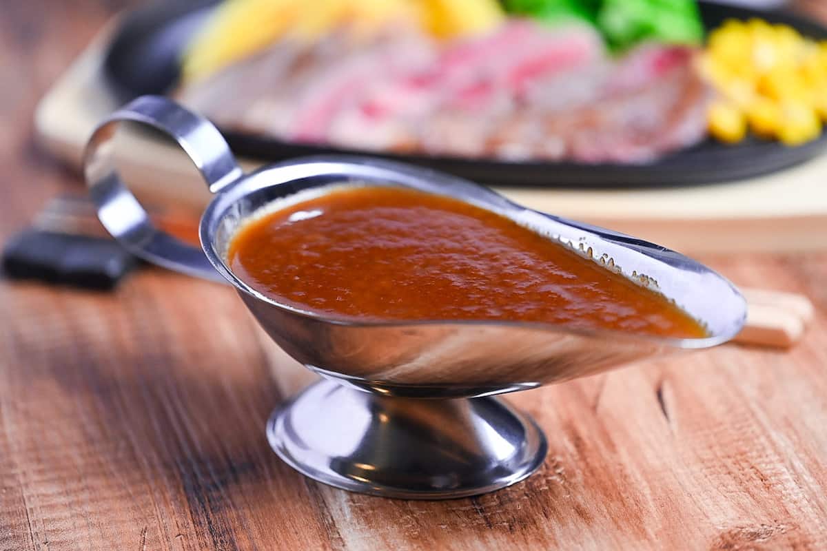 Japanese steakhouse style steak sauce in a steel gravy boat with slices of rare beef in the background