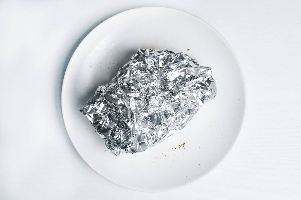 pan-fried duck breast wrapped in foil on a white plate
