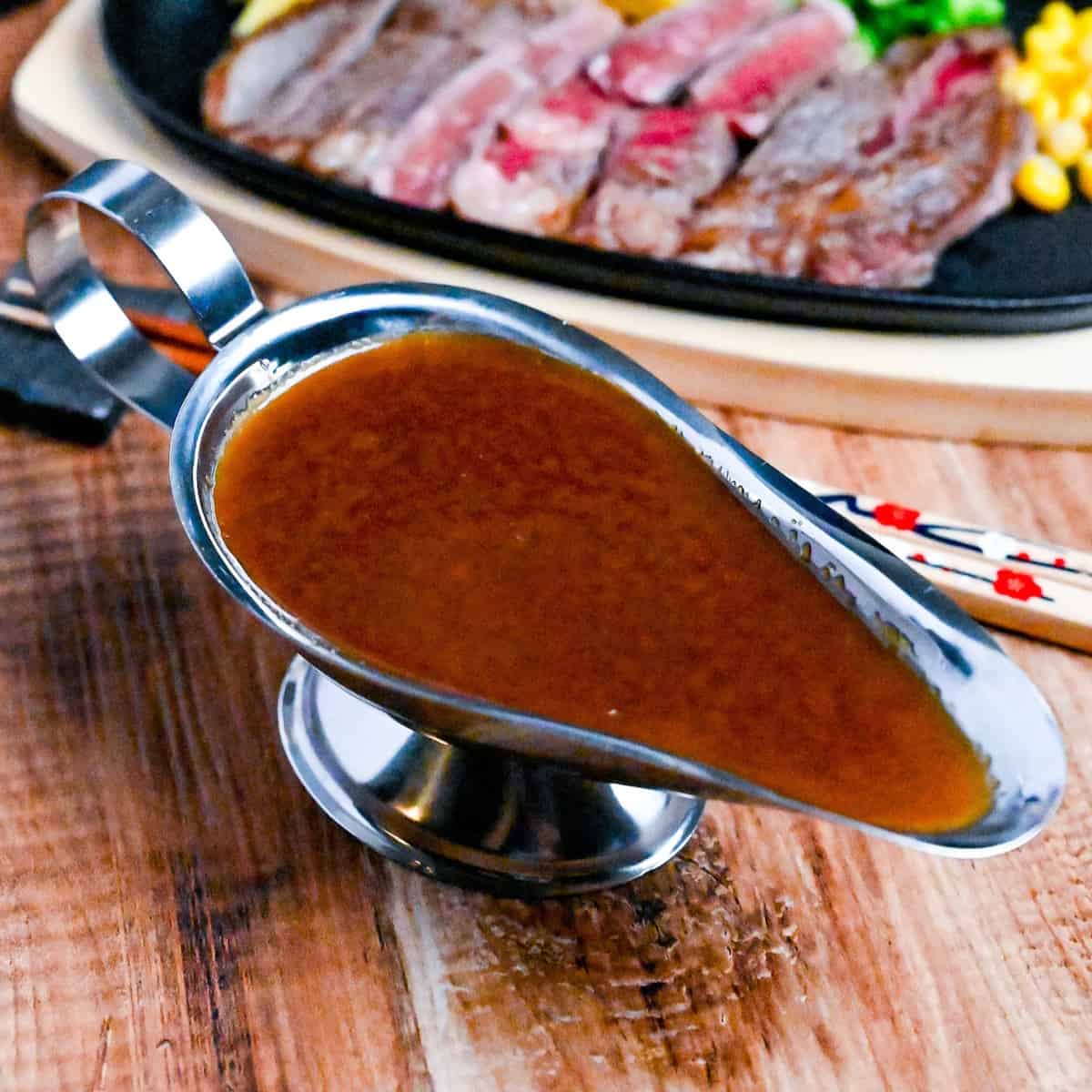 Japanese steakhouse style steak sauce in a steel gravy boat with slices of rare beef in the background