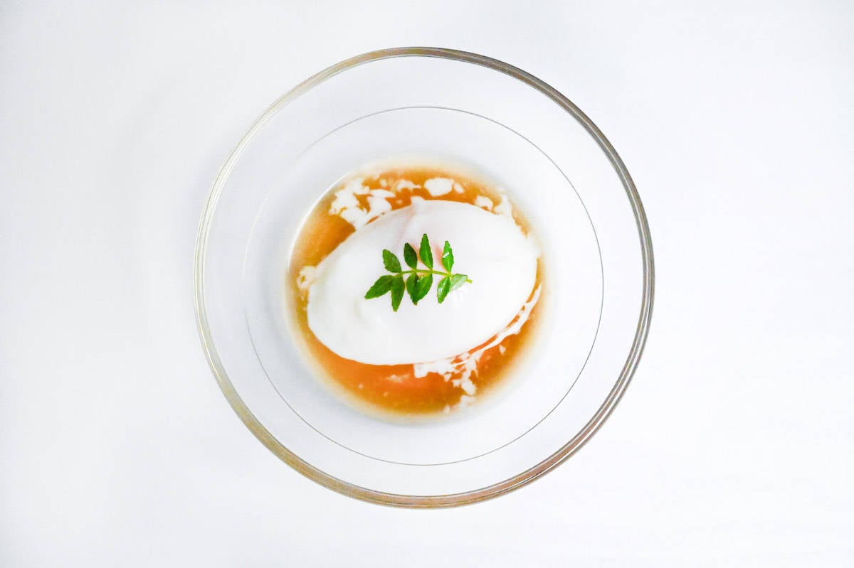 onsen tamago with sauce in a glass bowl topped with a leaf