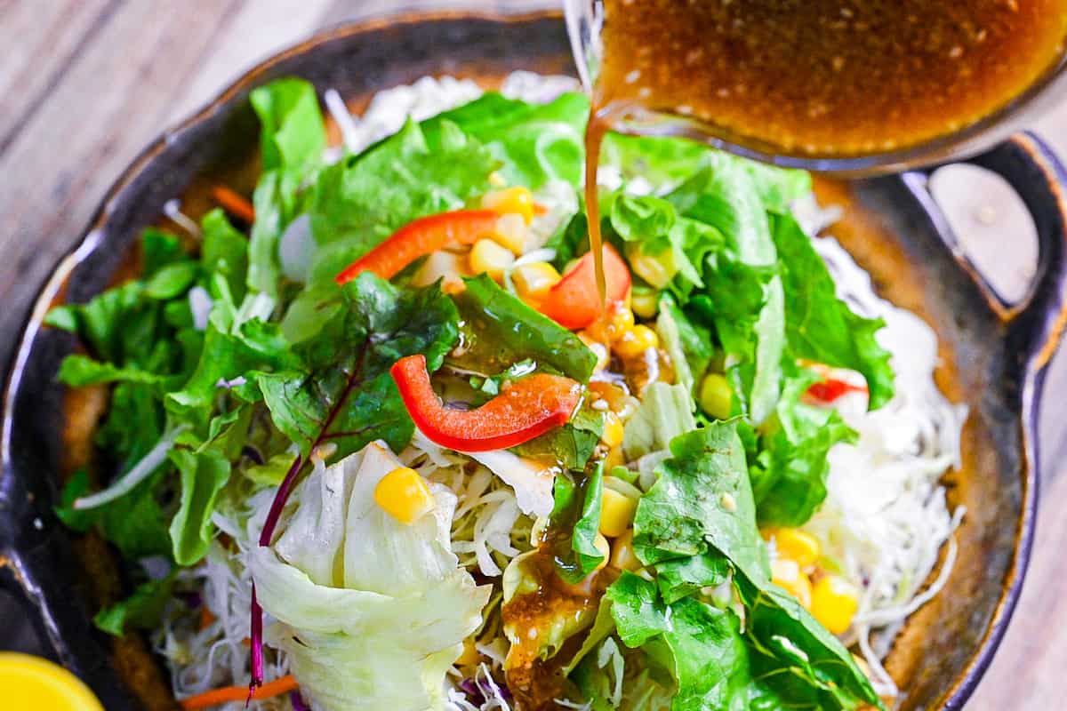 pouring ponzu dressing over a mixed leaf salad