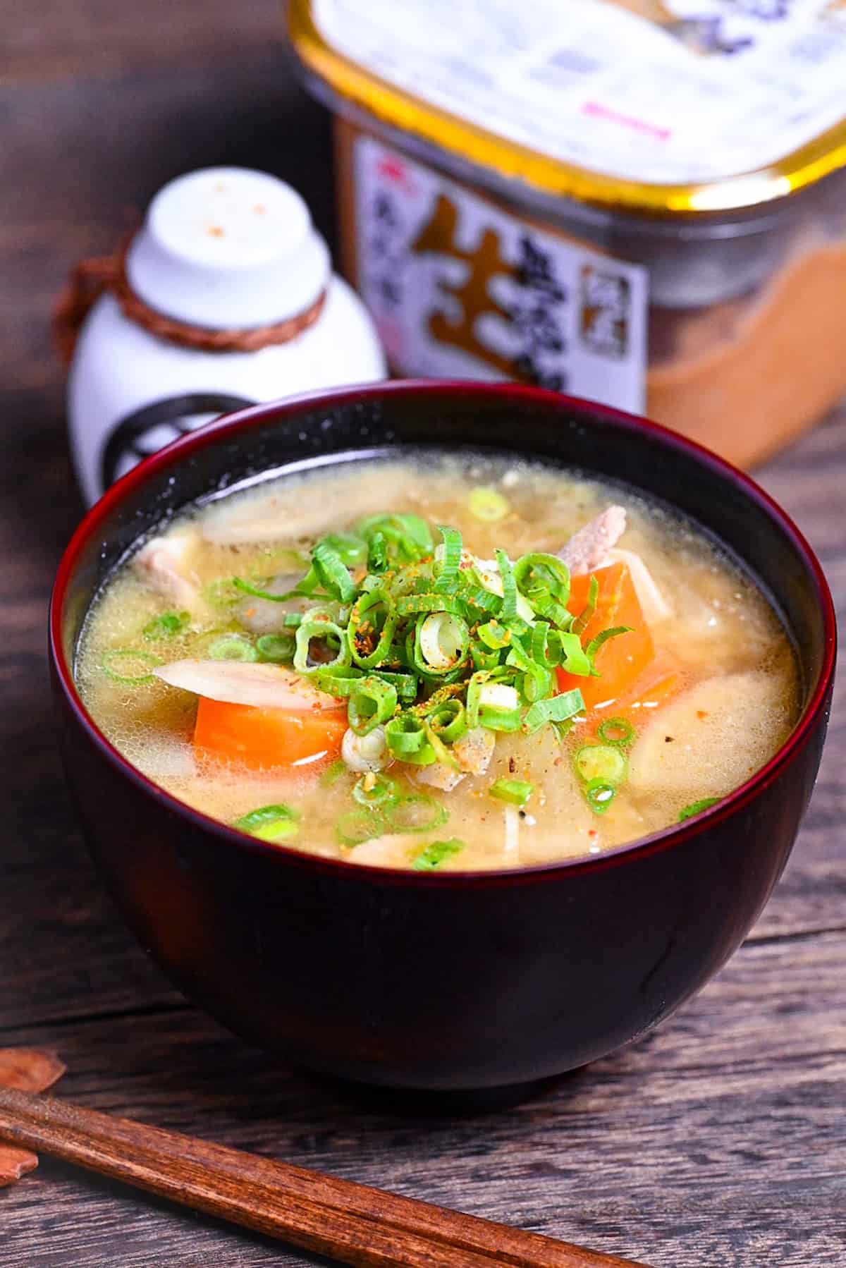 Japanese "Tonjiru" pork miso soup in a black and red bowl topped with shichimi togarashi (chili powder) and green onions