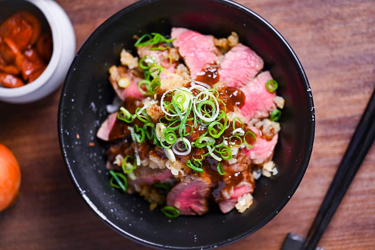 Chaliapin steak don made with slices of marinated steak cooked rare served over umeboshi and shiso rice and drizzled with an glossy gravy and chopped green onions