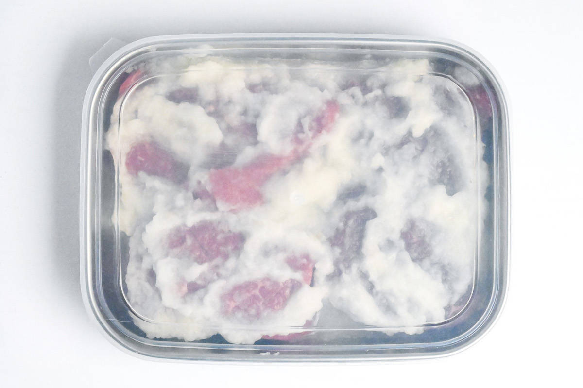 beef steaks in a steel container coated with pureed onion sealed with a lid
