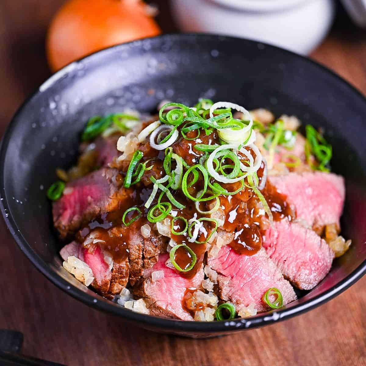 Chaliapin steak don made with slices of marinated steak cooked rare served over umeboshi and shiso rice and drizzled with an glossy gravy and chopped green onions