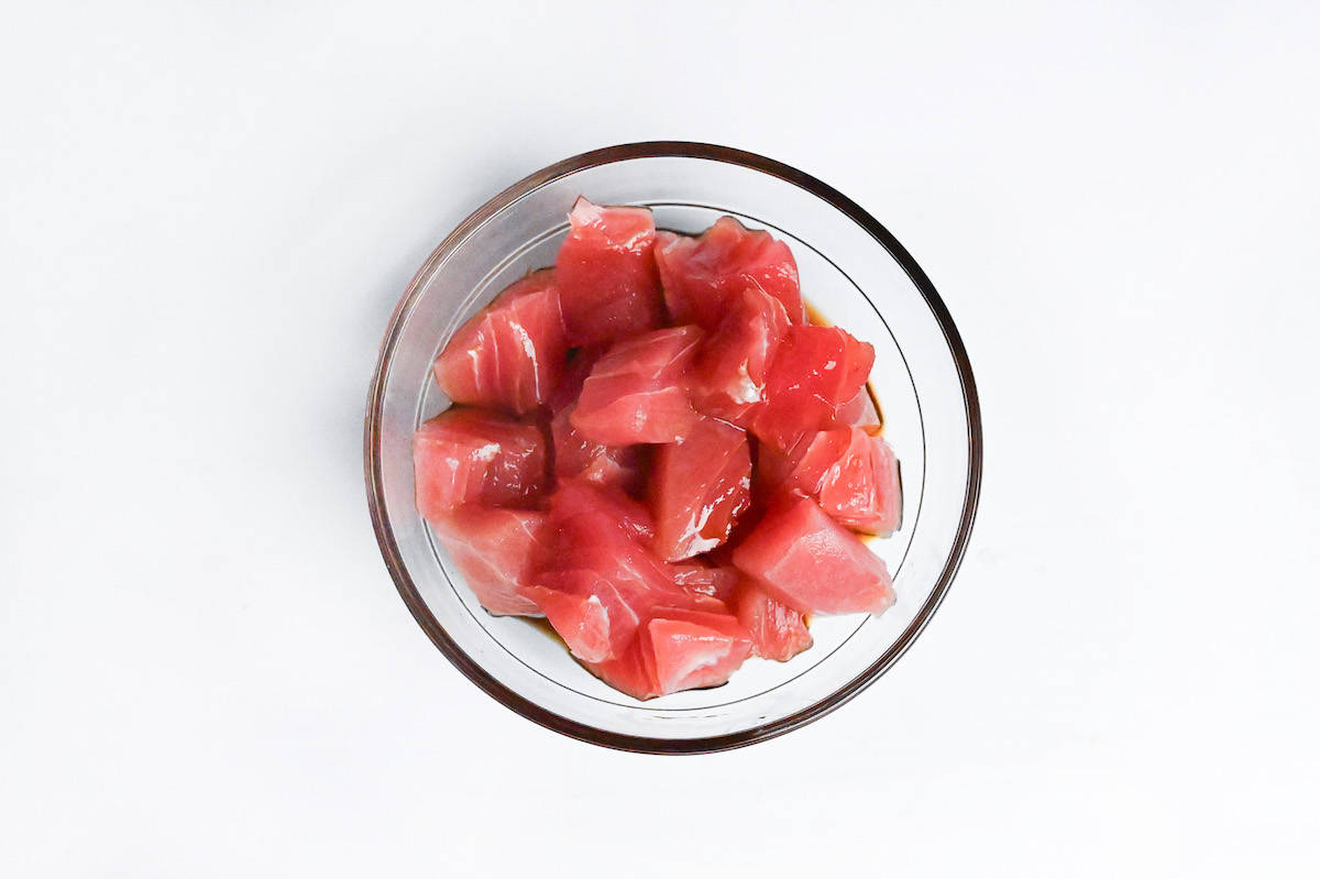 sashimi grade tuna cut into cubes and soaking in marinade in a small glass bowl