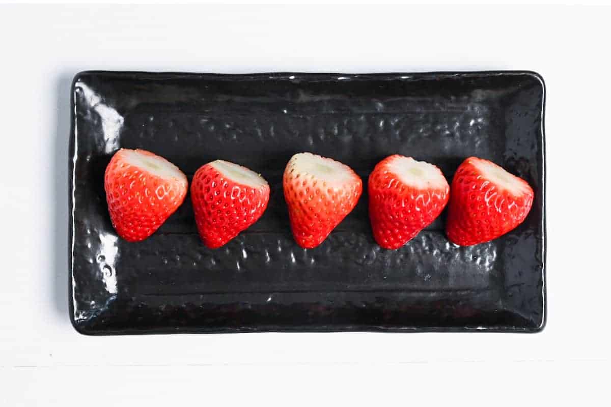 5 strawberries washed with stems removed on a black rectangular plate