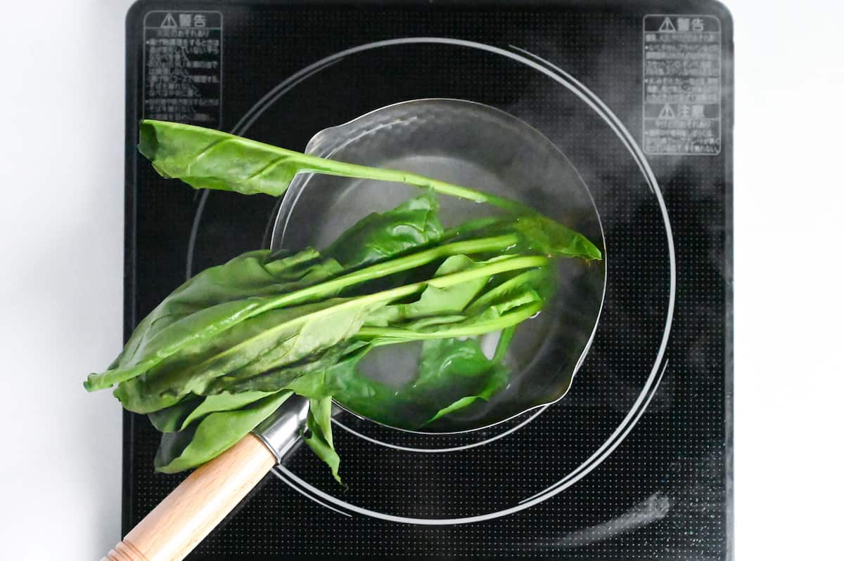 stems of spinach boiling in a pot with leaves sticking out