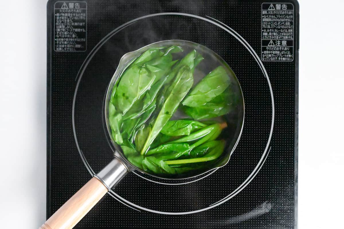 spinach leaves and stems submerged in a pot of boiling water