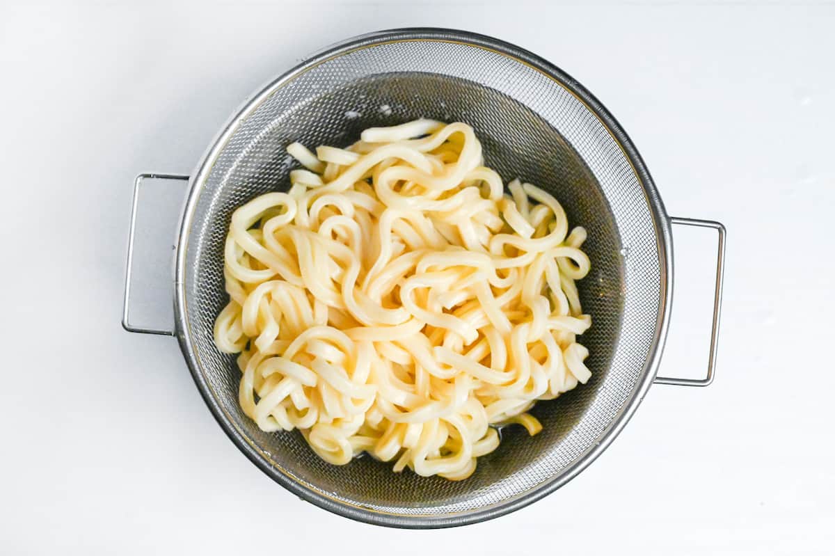 partially cooked udon noodles in a strainer over a bowl