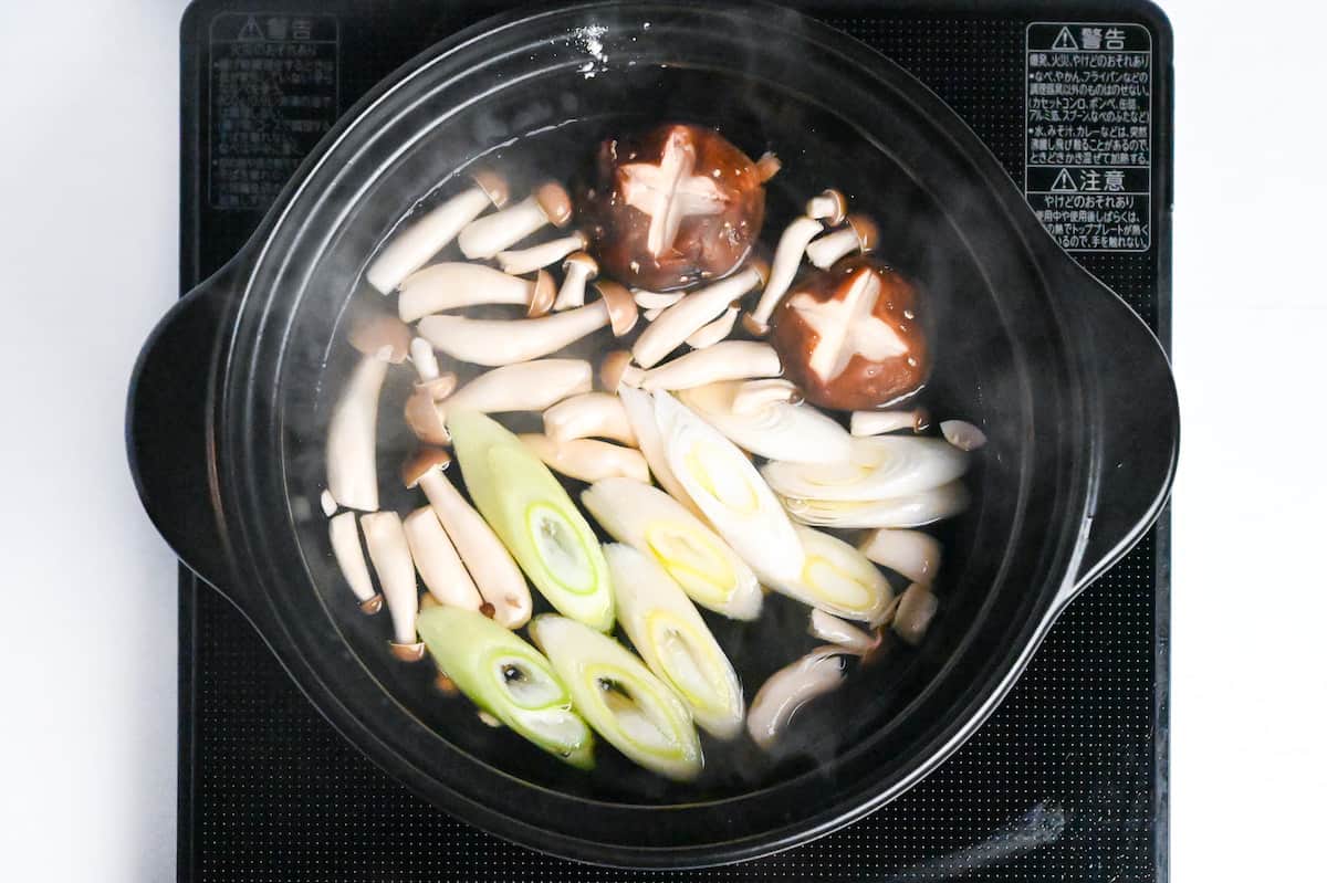 shiitake mushrooms, shimeji mushrooms and sliced green onion simmering in a black hot pot on the stove