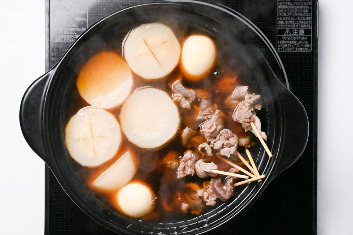 daikon radish and beef sinew skewers in oden broth in a black pot on the stove
