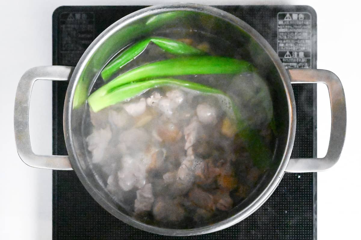 beef sinew, green onion and ginger in water in a pot on the stove