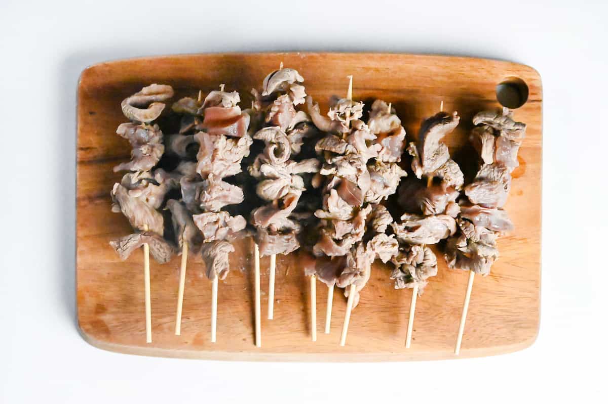 beef sinew pushed onto bamboo skewers on a wooden chopping board