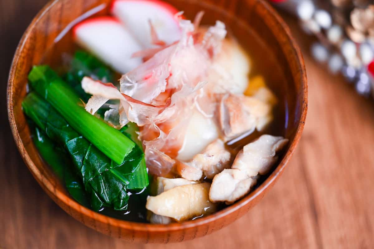 Nagoya style ozoni in a wooden bowl topped with slices of kamaboko (Japanese fishcakes) and bonito flakes