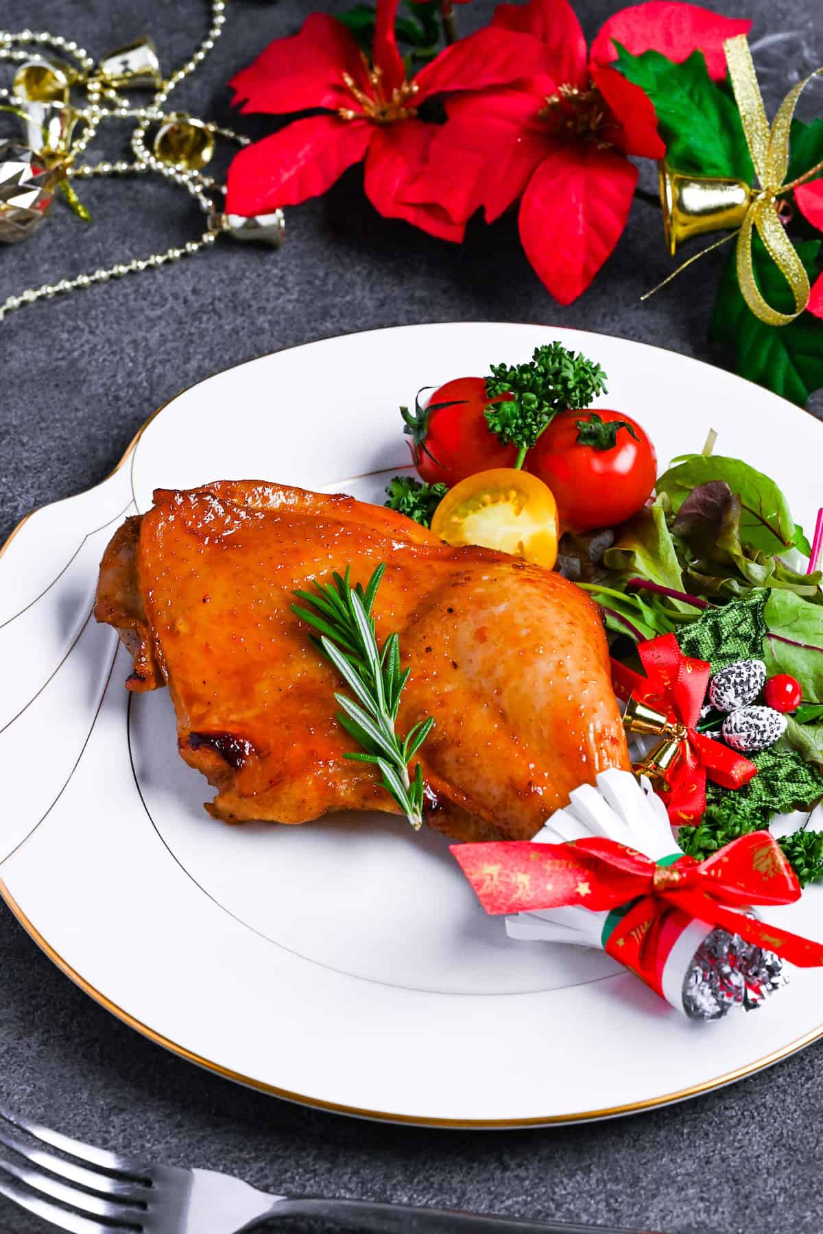 Japanese Christmas Chicken (Roasted Chicken with Soy and Yuzu Glaze) on a white plate topped with a sprig of fresh rosemary next to a simple side salad
