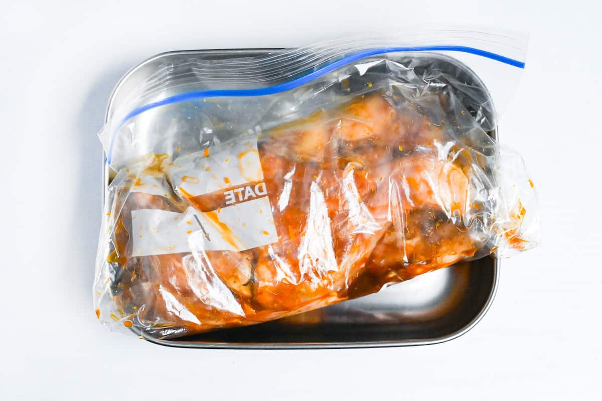 marinating two chicken leg quarters in soy and yuzu marinade in a sealed ziplock bag placed in a steel container