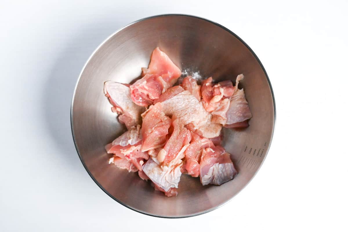 bitesize pieces of chicken thigh (skin-on) in a steel bowl sprinkled with salt and pepper