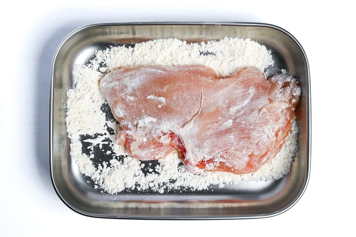 chicken breast coated in flour in a rectangular steel container