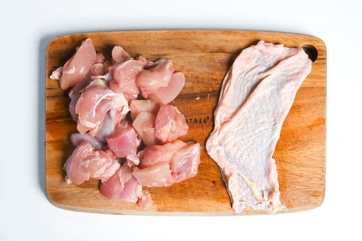 chicken skin and bitesize pieces of chicken thigh meat on a wooden chopping board