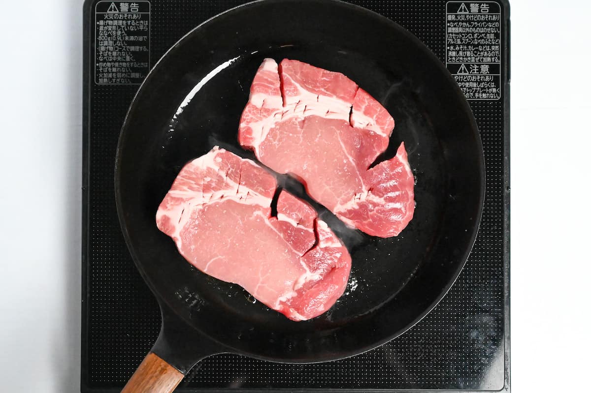 thick pork chops frying in a pan on the stove