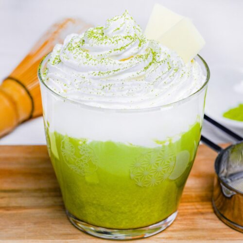 matcha white hot chocolate in a glass topped with whipped cream and two squares of white chocolate
