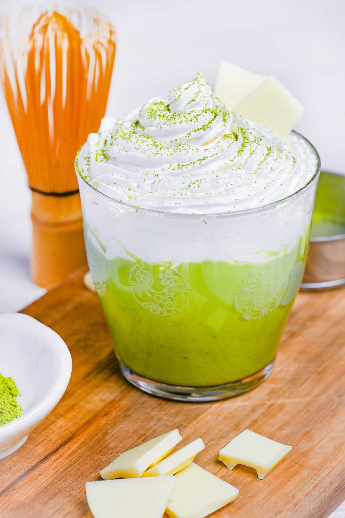 matcha white hot chocolate in a glass topped with whipped cream and two squares of white chocolate