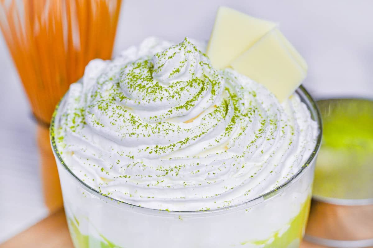 close up of whipped cream sprinkled with matcha powder on matcha white hot chocolate