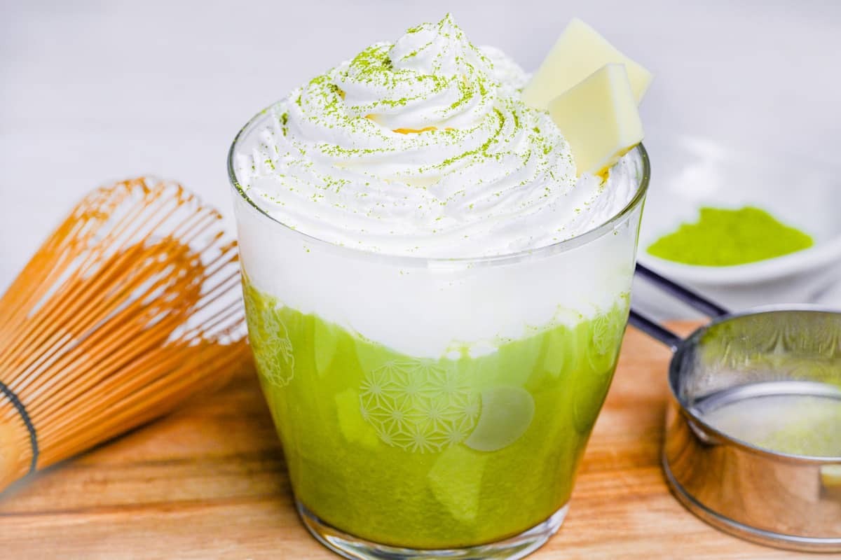 matcha white hot chocolate in a glass topped with whipped cream and two squares of white chocolate