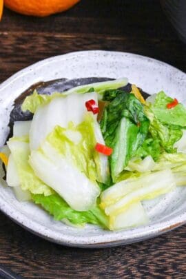 Japanese Napa Cabbage Pickles (Hakusai No Asazuke) on a small white plate with brown brushstroke design next to yuzu citrus and a bowl of miso soup