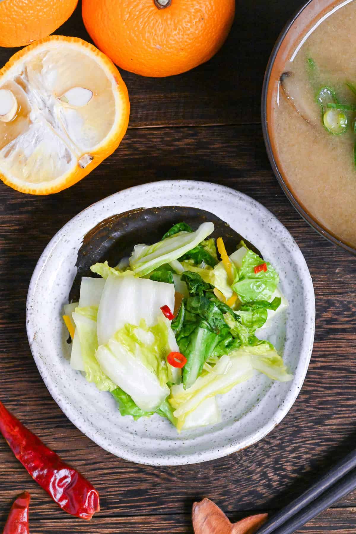 Japanese Napa Cabbage Pickles (Hakusai No Asazuke) on a small white plate with brown brushstroke design next to yuzu citrus and a bowl of miso soup