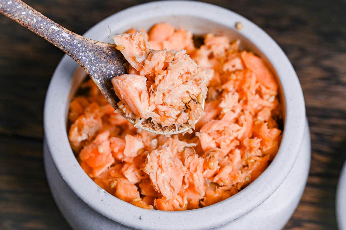 Homemade Japanese-style salmon flakes in a white ceramic pot close up with brown decorative spoon
