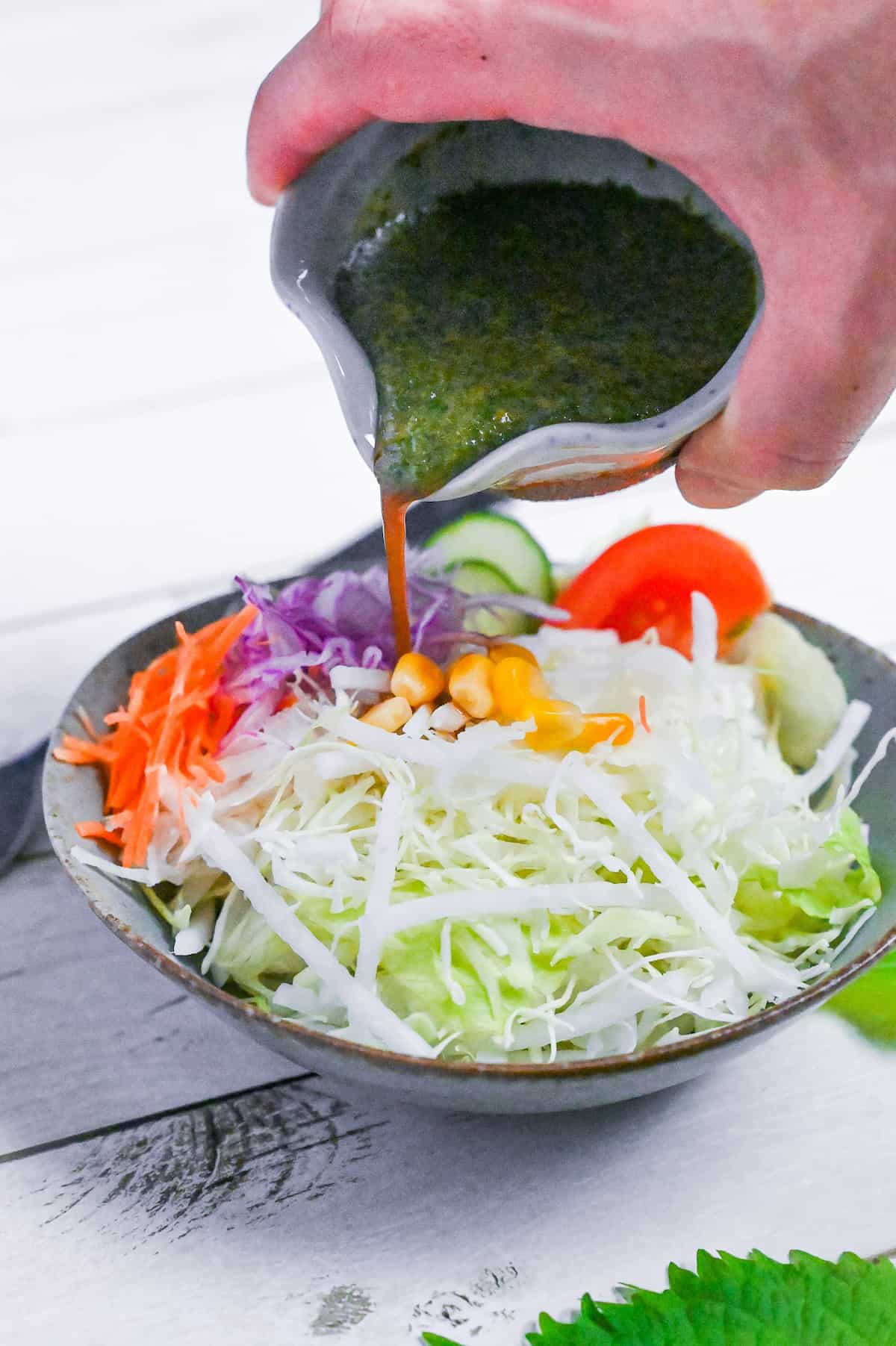 pouring Japanese shiso dressing over a mixed salad of crunchy lettuce, carrots, cucumber, tomato and sweet corn