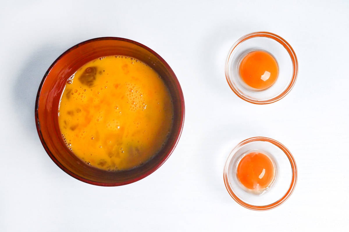 whisked egg in a bowl with two individual egg yolks in separate glass bowls