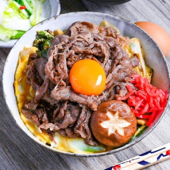 Sukiyaki beef donburi rice bowl topped with red pickled ginger, shiitake mushroom and egg yolk in a mottled bowl featured image