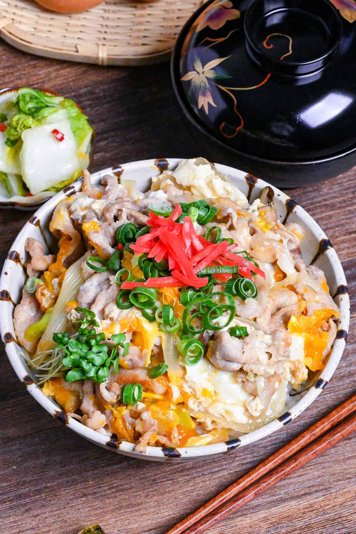 Tanin Don (Japanese pork and egg rice bowl) in a striped bowl topped with red pickled ginger and chopped green onions